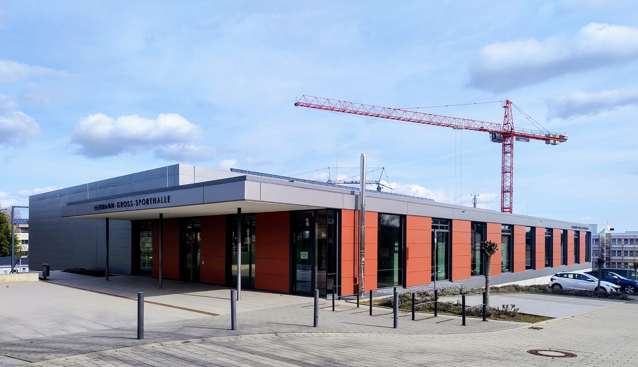 Flaches modernes Gebäude mit Schriftzug 'Hermann Gross Sporthalle' und rotem Baukran im Hintergrund. Das Foto ist in Birkenfeld Württemberg entstanden
