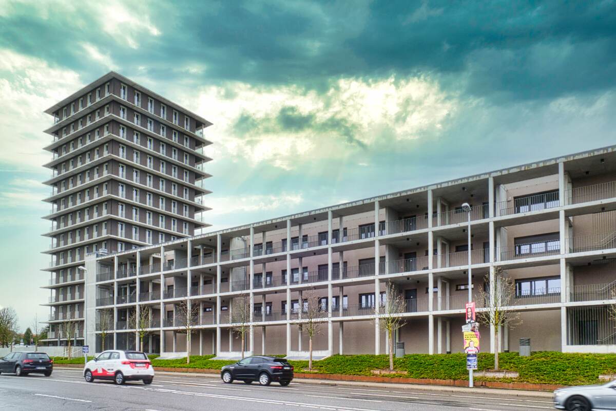 Hochhaus mit Holzfassade neben langgestrecktem Gebäude mit Balkonen an einer Straße mit mehreren Autos, Bweitragsbild für Immobilienvermittlung in Pforheim Arlinger und Brötzingen durch schwebius-immobilien