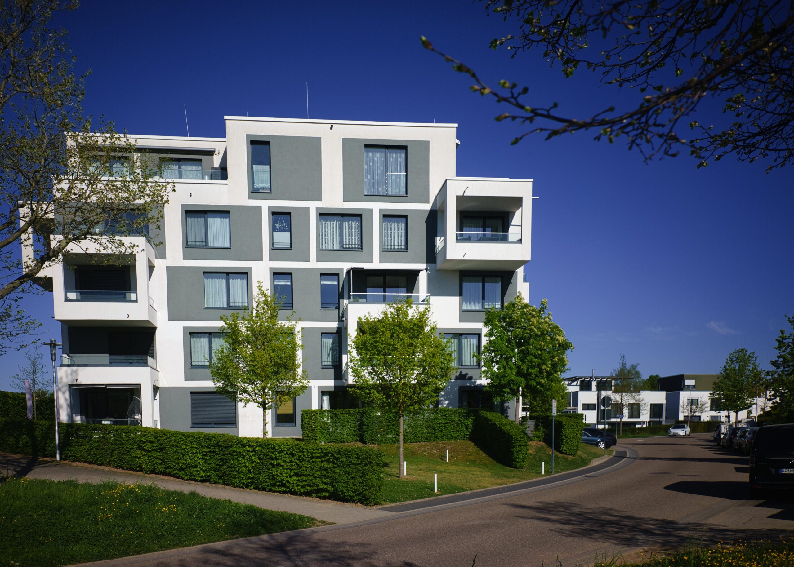 Mehrstöckiges Wohngebäude im Bauhausstil mit klaren Linien, großen Fenstern und Balkonen, umgeben von Bäumen und einer Straße