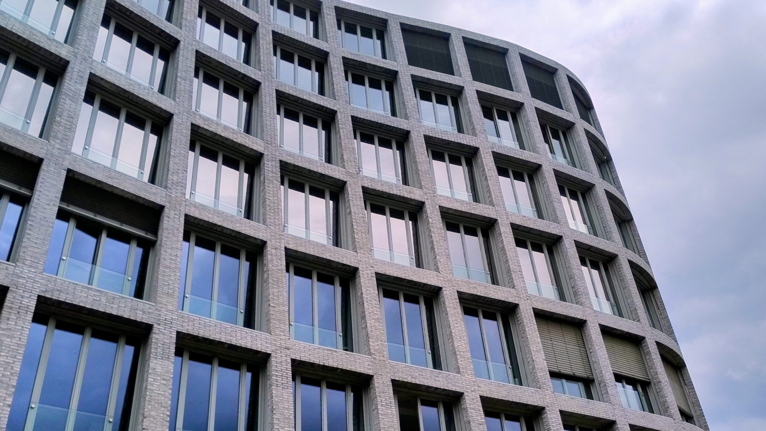 Bürogebäude mit regelmäßigen Fensterreihen und grauer Fassade unter bewölktem Himmel